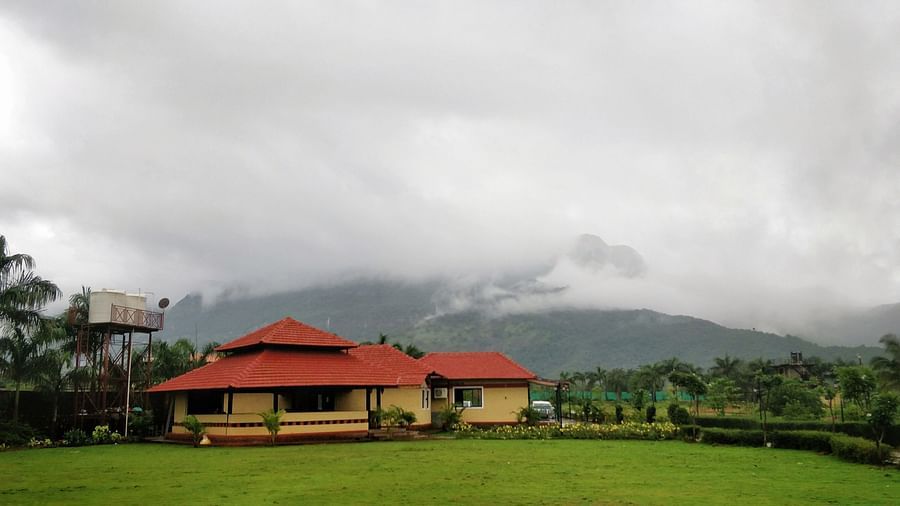  A lush green field with a house and trees in the background, under a grey and cloudy sky | The Kanila Resort