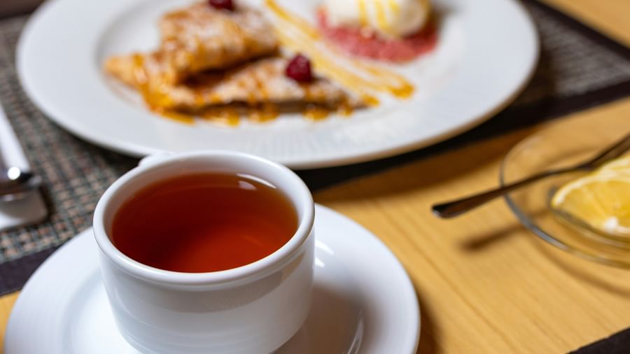 Close up view of a cup of tea with a side dish served on a breakfast table at Fireflies Resorts, Kabini.