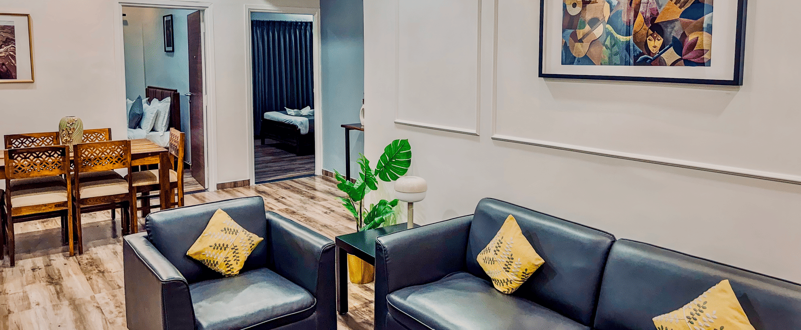 Separate living room of Coral 4BHK at Kove Smart Stays furnished with upholstered multi-seater sofas, a wooden dining table, and doorways leading to inner rooms.