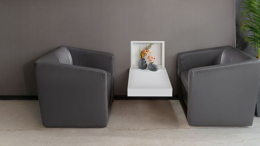 A minimalist and inviting lounge area at The Atara, Gurugram is furnished with two comfortable armchairs, a small side table, framed artwork adorning the wall, and a green plant
