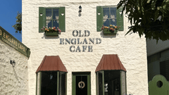 The facade of two-storey Old England Cafe at Hotel Atulyaa Taj, Agra on a sunny day under a clear sky with a couple of tables placed outside