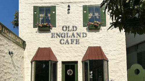 The facade of two-storey Old England Cafe at Hotel Atulyaa Taj, Agra on a sunny day under a clear sky with a couple of tables placed outside
