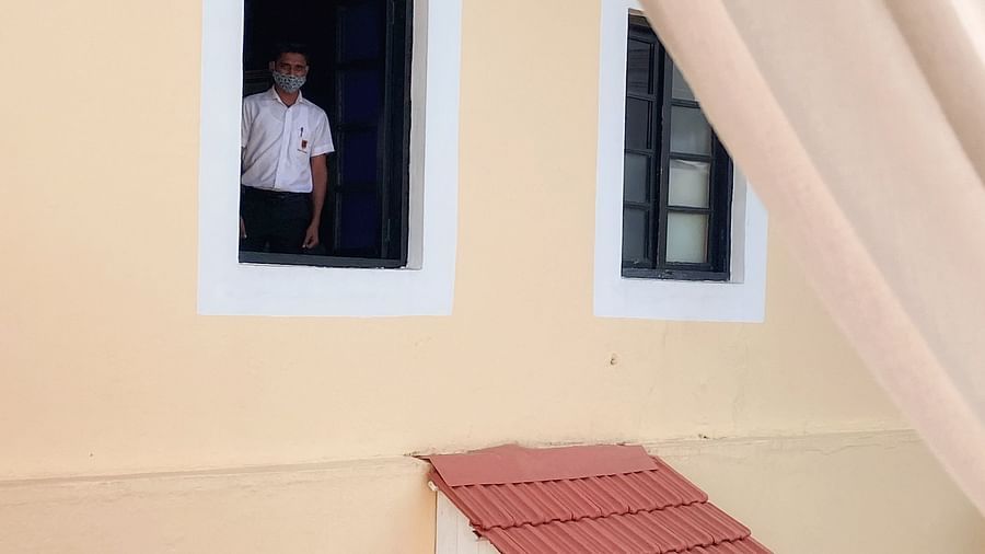  A person in a white shirt looks out from an open window on the upper floor of a yellow building with white trim and a red awning, at Fort Tiracol, Goa. 