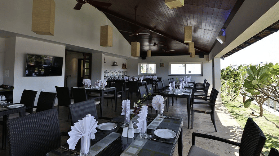 The spacious covered rooftop dining area in Tree Top Restaurant with arranged table settings, folded napkins, and outdoor balcony plants at Temple Tree Hotel, Bangalore.