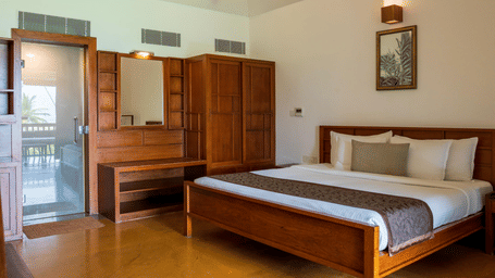 A hotel room featuring a double bed, a wooden wardrobe with a vanity mirror, and a glass door leading outside | Le Pondy