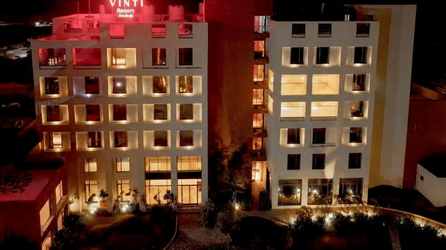 The main building of Vinti Resort, Ambaji, illuminated at night, showcases the warm glow from the guest rooms and lobby.