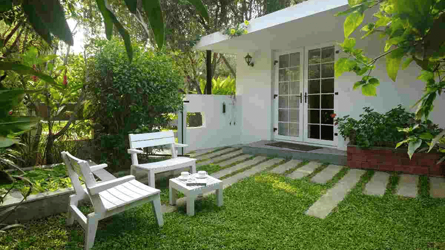 White cottage with a private garden, outdoor seating and a stone pathway surrounded by greenery at Amanvana Spa Resort, Coorg.