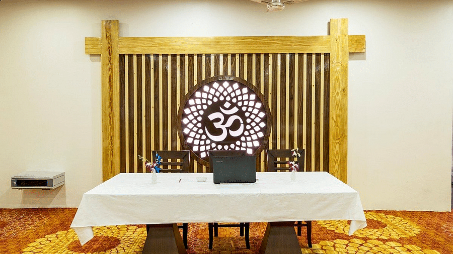 A table with a white table cloth spread over it with two chairs behind it in the Banquet Hall at Regenta Inn DLS.