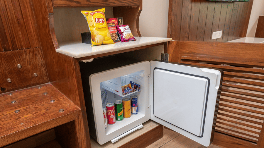 In-room minibar at Quality Inn Dharamshala featuring an open mini refrigerator stocked with snacks and beverages fitted within a wooden cabinet unit.