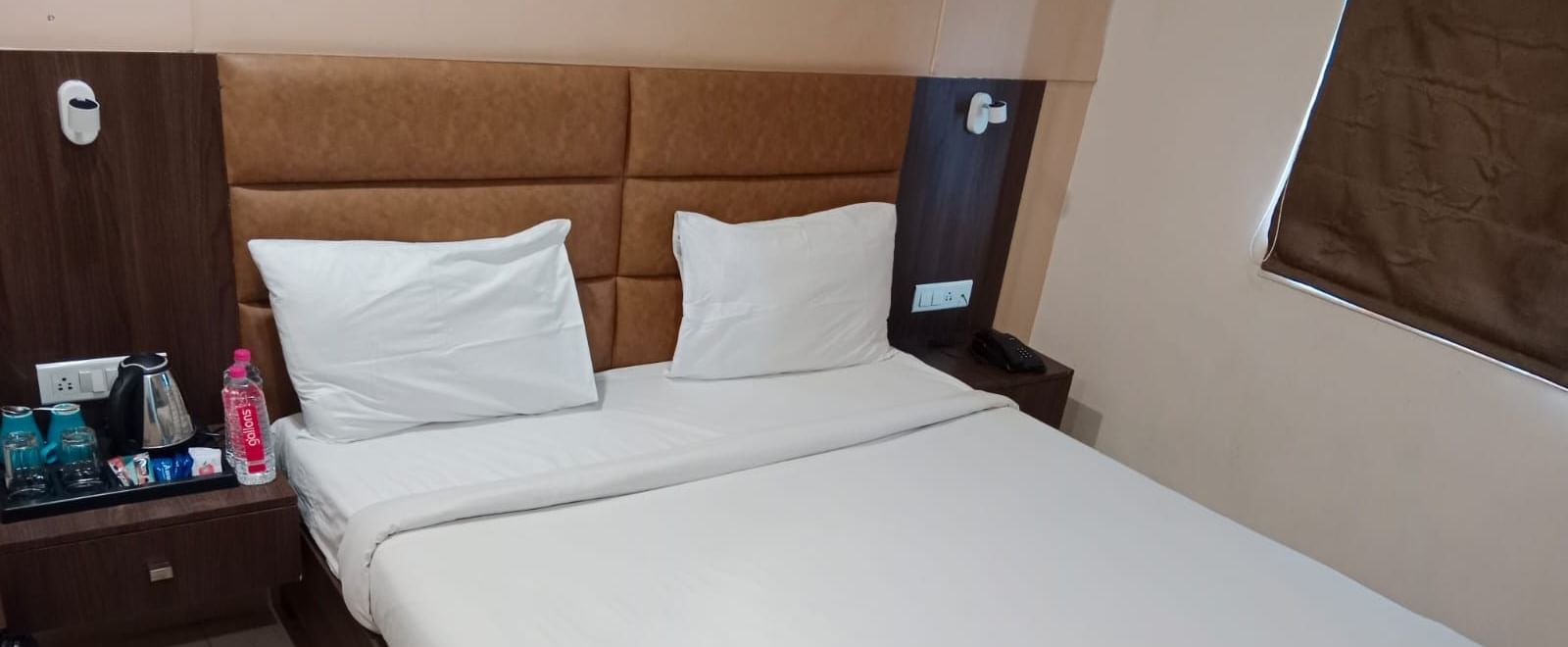 Top view shot of  double bed in the Deluxe Room at Pravasa Ahmedabad with bed side tables on either side of the bed.