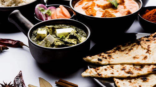 Selection of Indian dishes including naan, curry, and soup served in black bowls and plates.