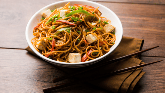 Bowl of stir-fried noodles with chopsticks placed on a wooden surface, representing Asian cuisine.
