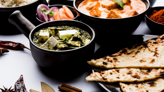Selection of Indian dishes including naan, curry, and soup served in black bowls and plates.