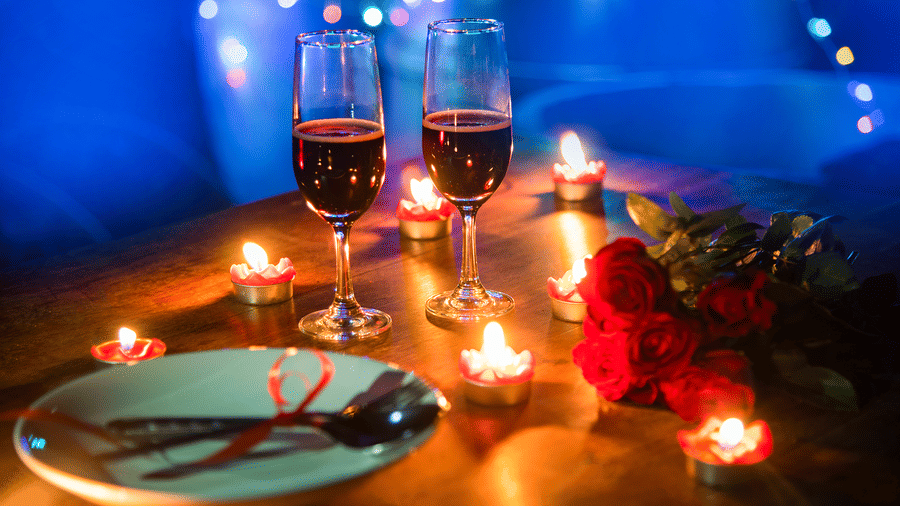 Romantic dinner setup with wine glasses, candles, and rose petals, creating an intimate ambiance.