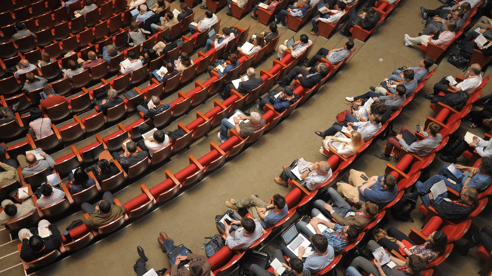 High-angle view of a large audience seated in rows of red theatre chairs during an event or performance.
