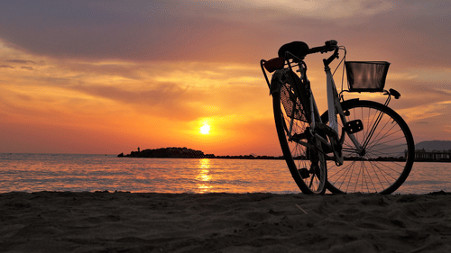 a cycle parked on the beach with the sun setting in the background