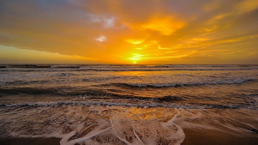 Beach waves at the shore with the sun setting in the background