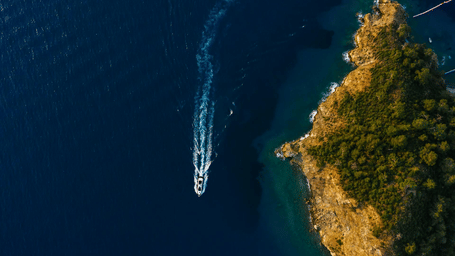 Aerial view of a speedboat moving through deep blue water near a rocky island.