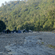 A dry rocky riverbed with small streams surrounded by forested hills and a distant campsite.