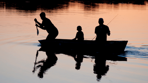 silhouettes of two adults and a child on a boat rowing to reach a destination 