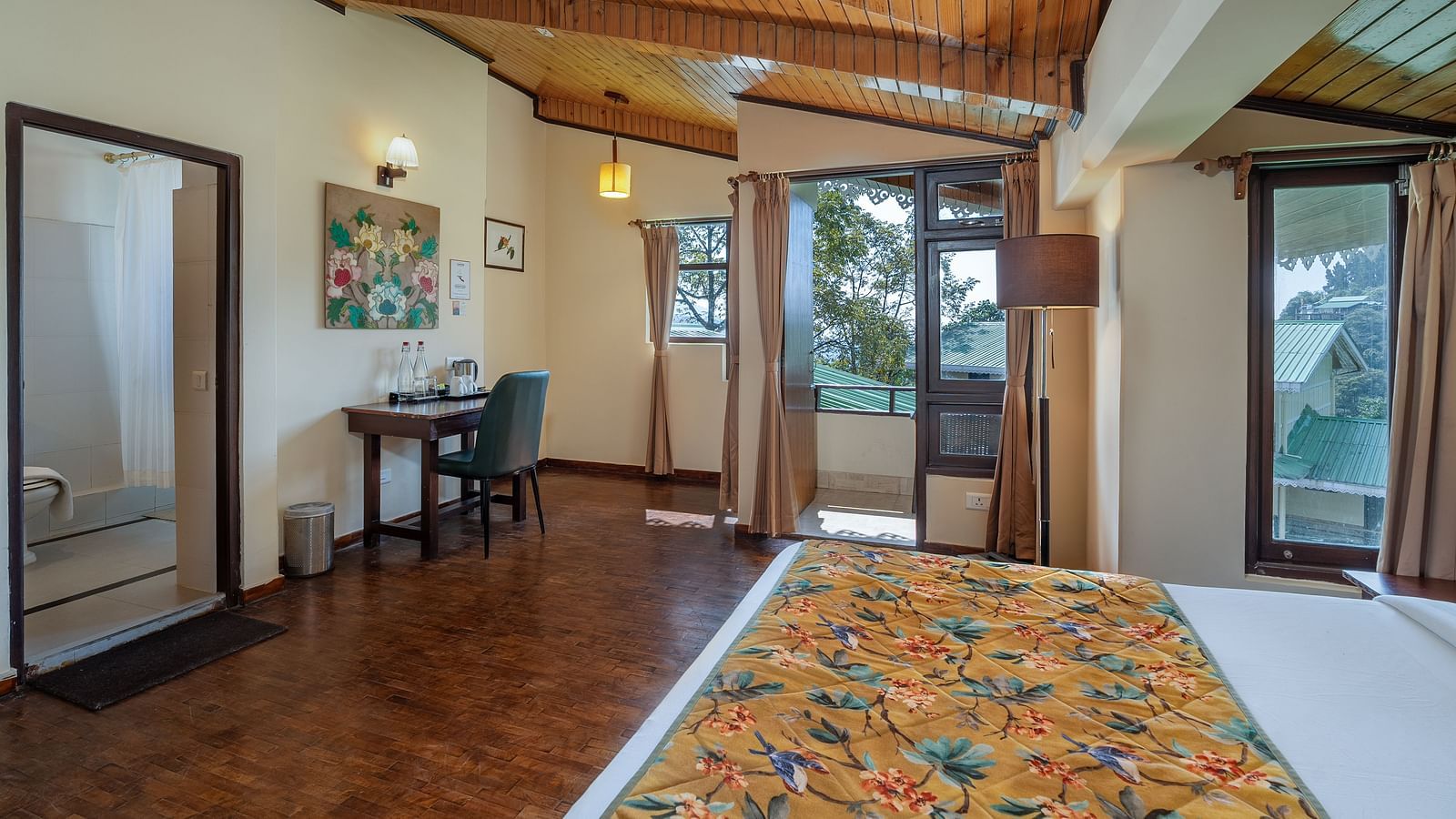 Deluxe room featuring a spacious bed, wooden table with a chair, a large doorway to the bathroom, and a balcony with side curtains at Summit Norling Resort & Spa, Gangtok
