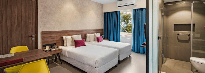 One of our rooms in thoothukudi with twin beds, a table with yellow chairs, and a modern shower area in front - Regency Tuticorin by GRT Hotels