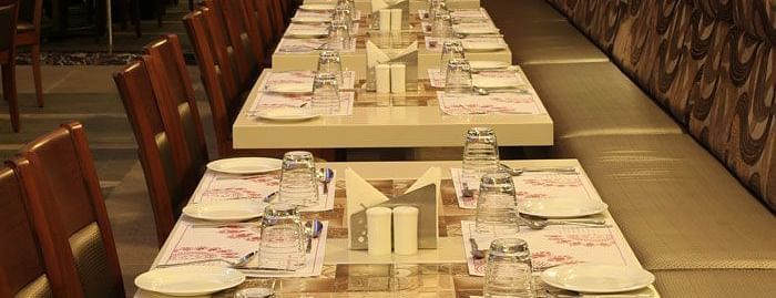A long dining table set with fine cutlery and napkins, perfect for group dining and special occasions. - Dhanalakshmi Srinivasan Hotels, Perambalur