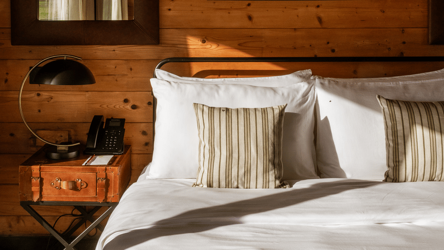 A close-up vertical shot of the bedside area at Rhino & River Wildlife Retreat & Spa, Pobitora, highlighting the warm timber walls and minimalist decor.