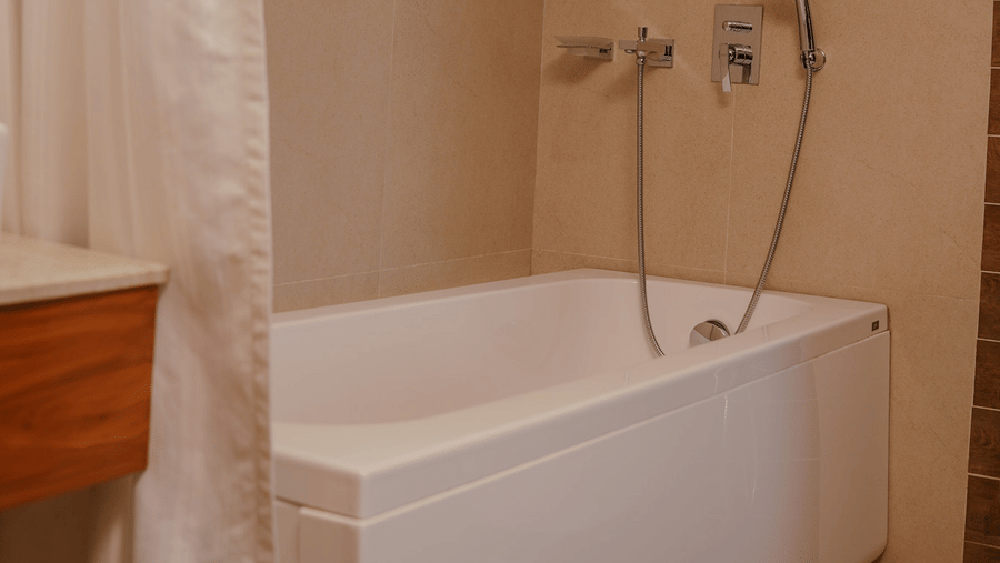 A beige bathroom features a white rectangular bathtub with a handheld shower head and a fabric curtain at Tiara by MPS.