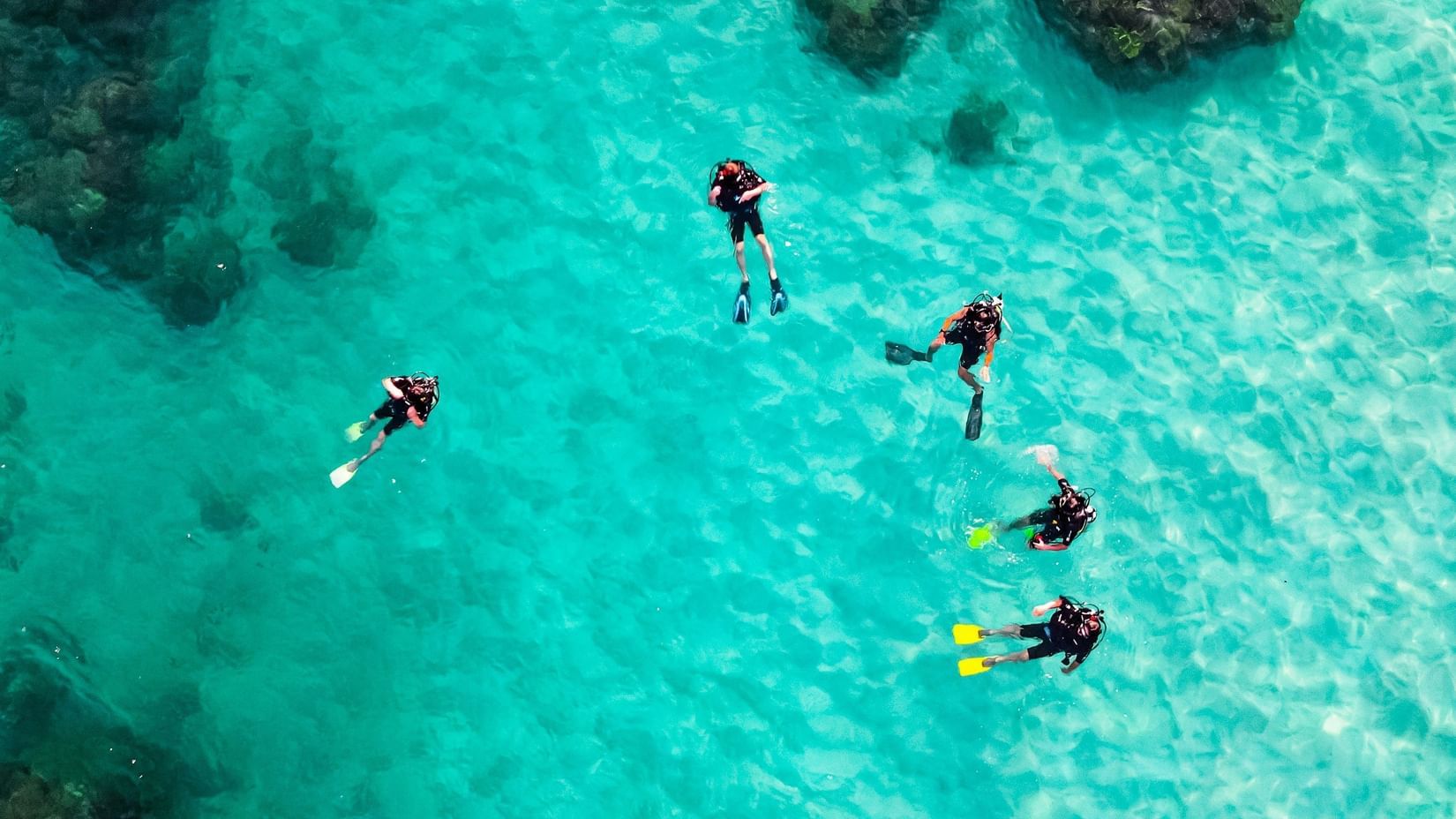 Aerial view of snorkelers or swimmers exploring clear turquoise waters near a reef.