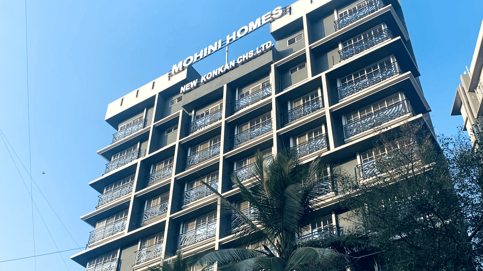 Low-angle view of the multi-storey Home2 Residency, Mumbai Airport, building facade against a bright blue sky.