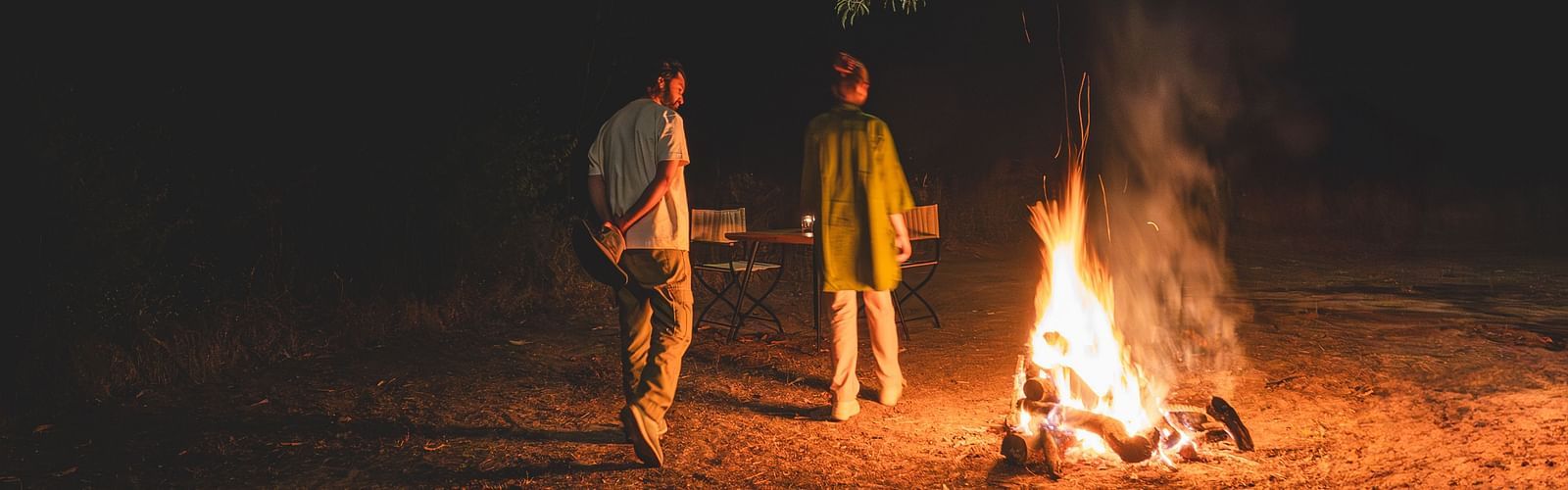 Two people walking around a bonfire at Trees N Tigers, Tadoba.