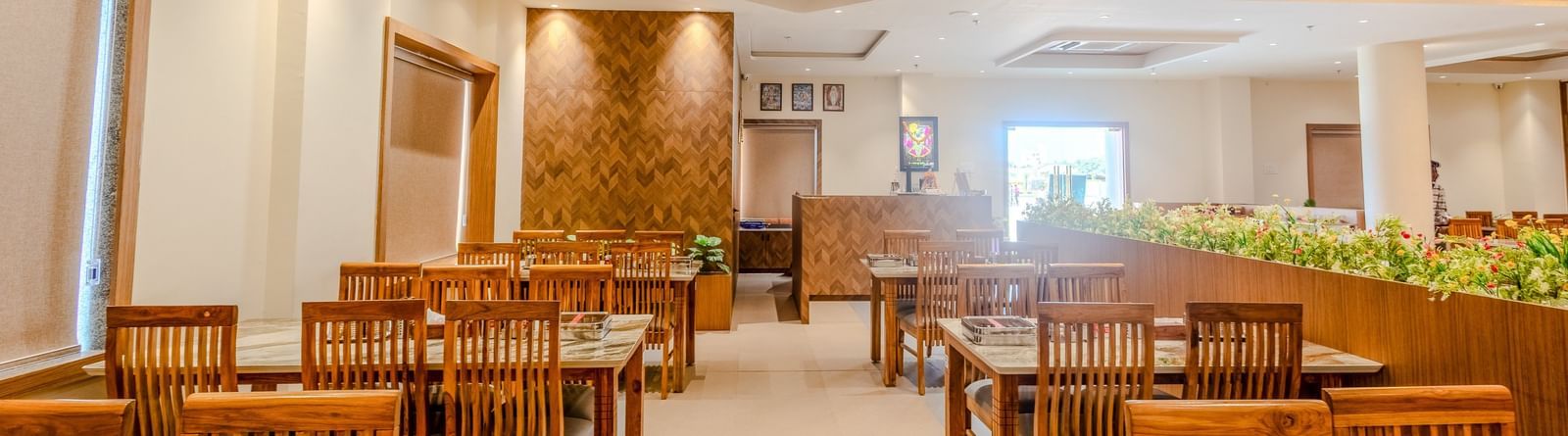 Interior of the dining area at Daksh The Grand Gowardhan, Dwarka, featuring wooden tables and chairs, with warm lighting.
