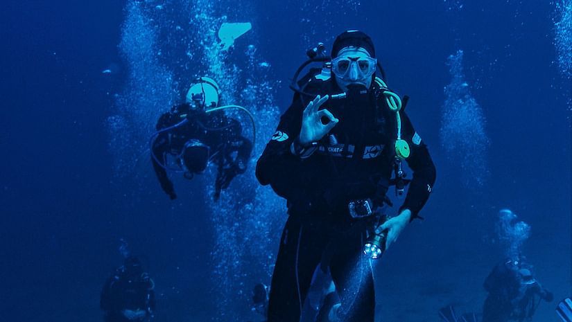 Divers exploring underwater with bubbles around them, near a submerged structure