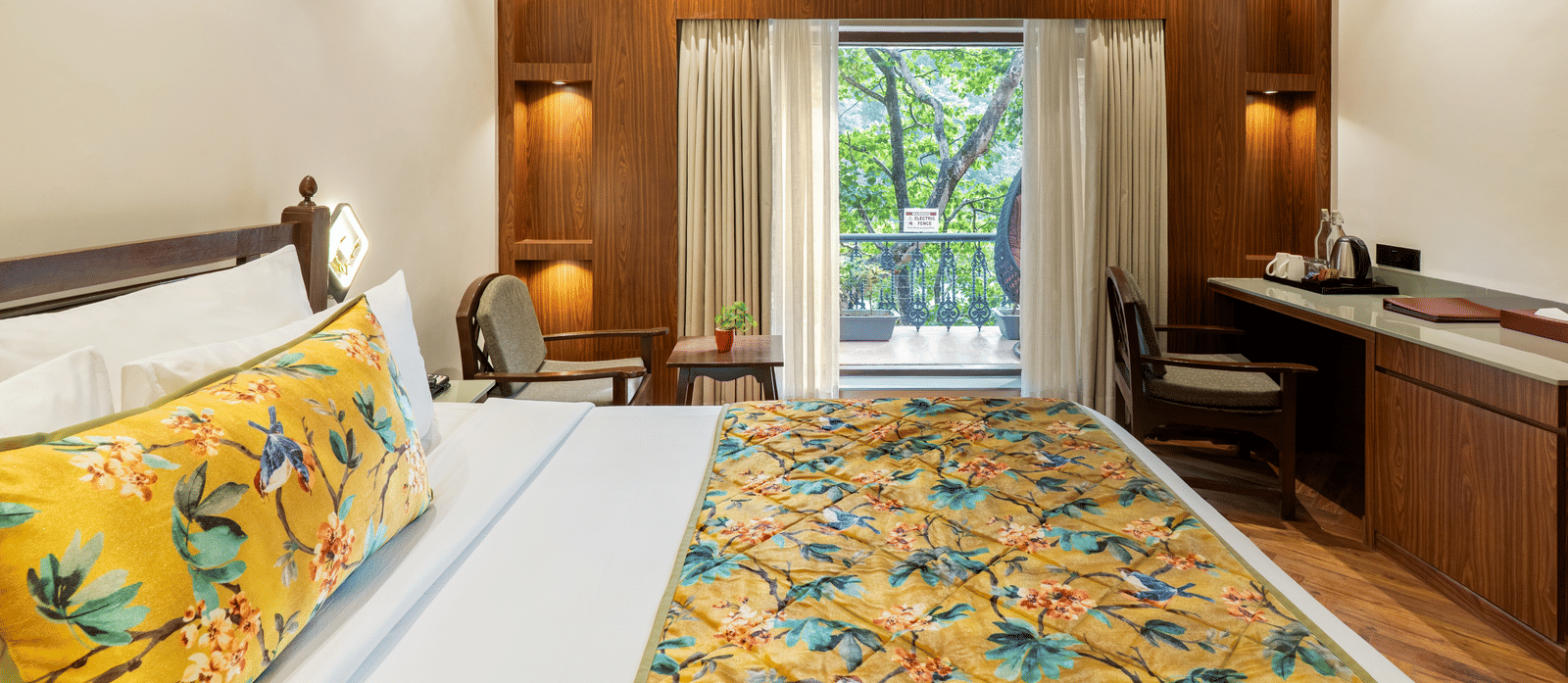 A bedroom featuring a big bed, 2 wooden chairs, an A/C unit, an attached balcony with a standing swing chair, potted plants, and view of the trees outside | Summit by the Ganges Beach Resort & Spa, Rishikesha