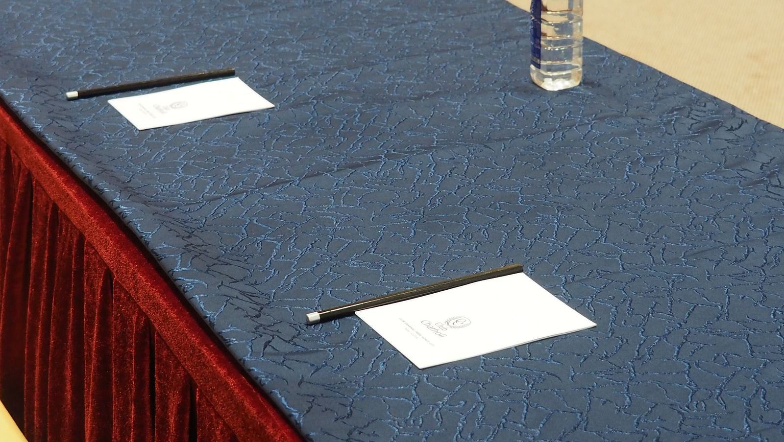 A close-up of a blue table with water bottles and paper, draped in red cloth - Club Charholi, Pune 