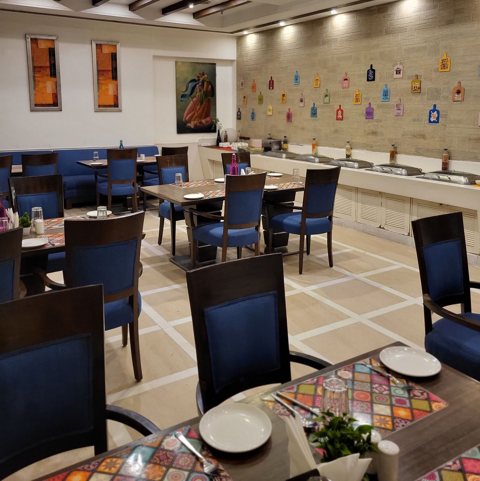 An image of a restaurant featuring multiple sets of chairs and tables where plates, cutlery and napkins are placed at Inde Hotel Signature Tower Gurgaon
