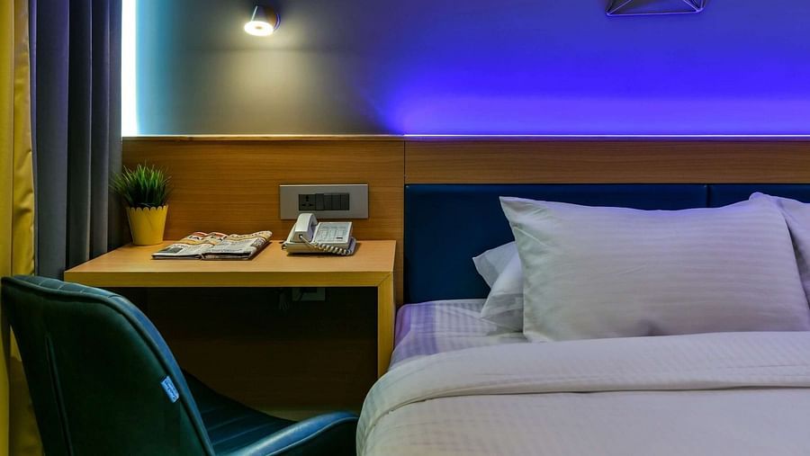 A spacious bed with a wooden work desk and chair placed beside it, accompanied by a night light above, at Indie Stays, BKC Kalina.