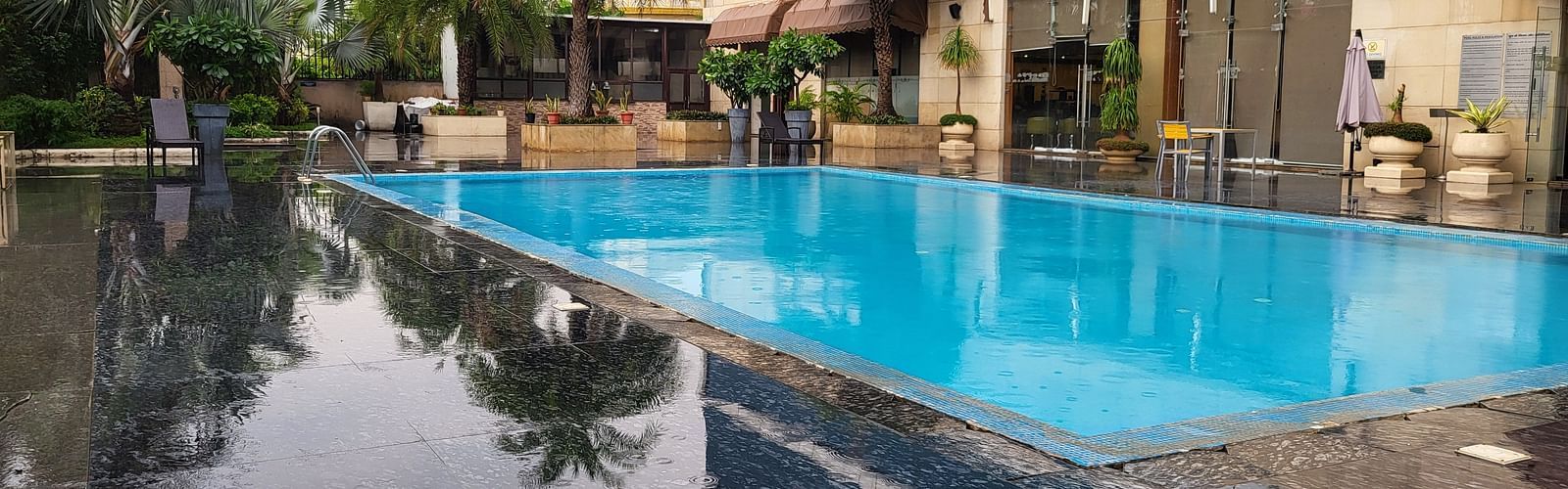 An image of a swimming pool surrounded by some palm trees in the property of Golden Suites Gurgaon