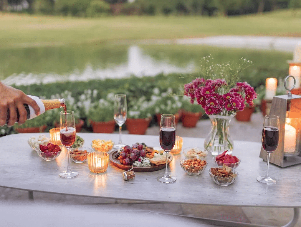 Dessert table setup near a lake with candles, pink flowers, and an assortment of sweets in glassware at Karma Chalets.