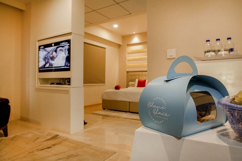 Sitting area of the suite room with a packet of food on the table, a television mounted on the wall and door leading to the bedroom  Art Boutique Hotel, Hyderabad