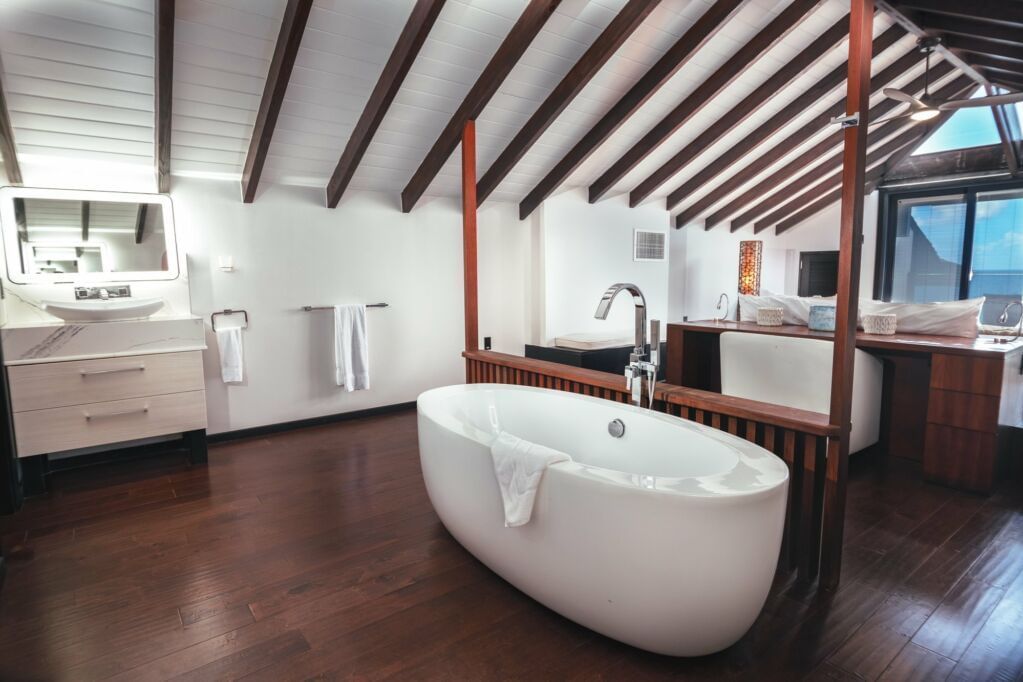 Spacious modern bathroom with a freestanding bathtub, wooden flooring, and vaulted ceiling with exposed beams.