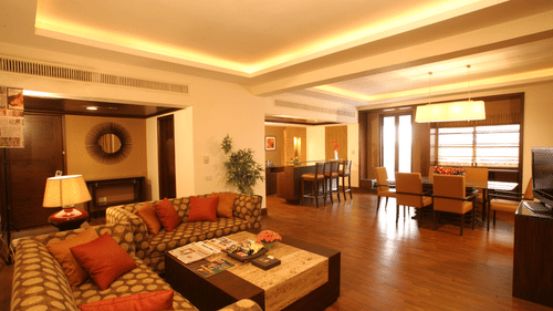 A hotel suite with sofas, tables, chairs, and warm lighting in the living area.
