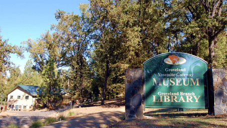 A sign reading Groveland Yosemite Gateway Museum and Groveland Branch Library surrounded by trees on a bright sunny day.