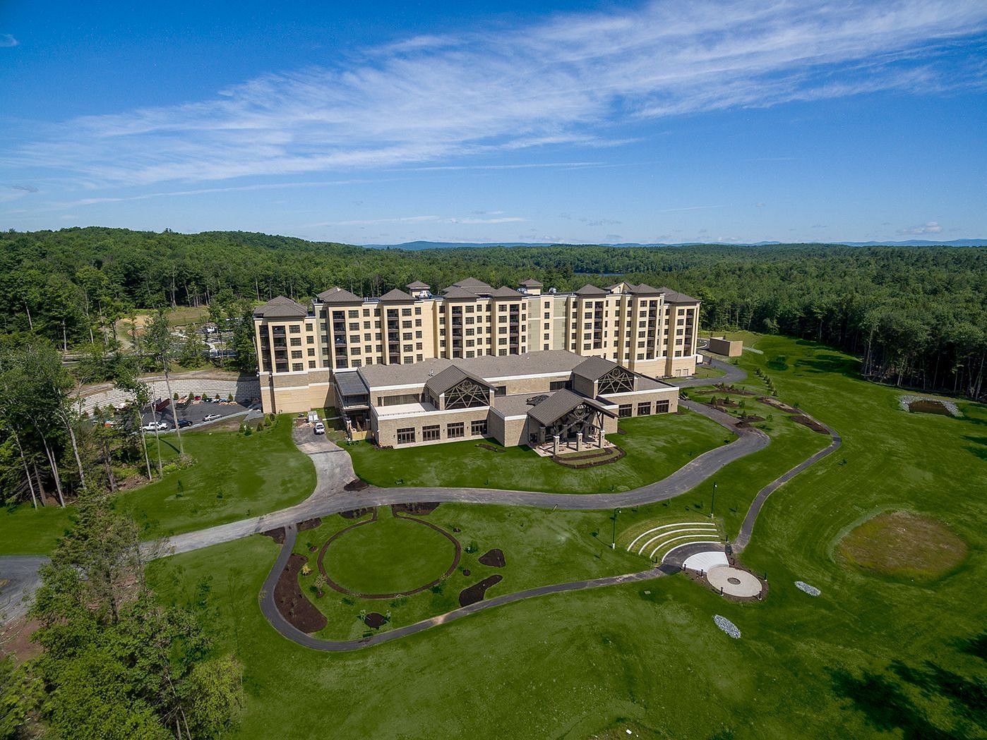 The facade of YO1 Longevity and Health Resorts in Catskills with various wings, surrounded by vast green lawns and dense forests under a clear blue sky. 