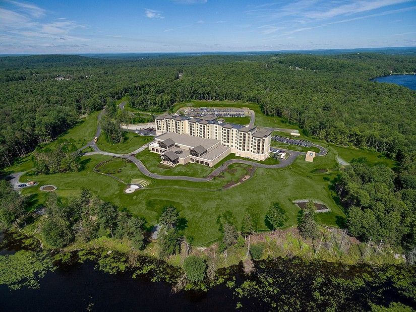 aerial view of YO1 Longevity and Health Resorts amidst vast green lawns and dense forests, with winding pathways and a large body of water in the distance. 