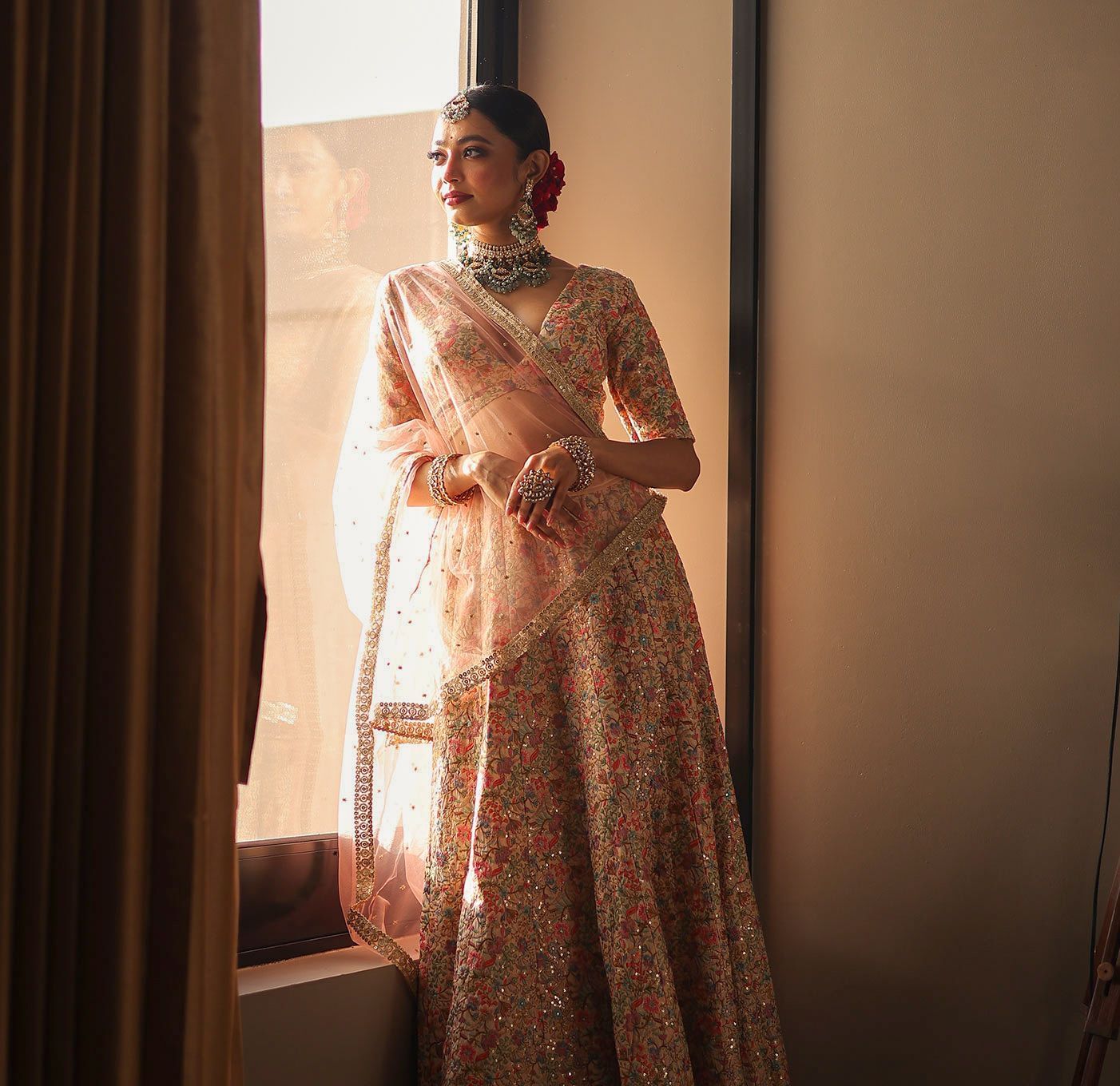 A woman in Indian bridal attire leaning against a glass window - Polo Hotel Agartala