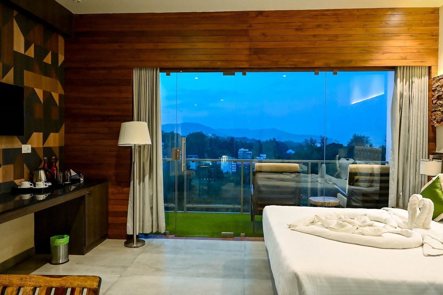A hotel bedroom with a large bed, a bedside lamp, and an expansive view from a large glass door, suggesting access to a private balcony or terrace - Sea Hills Hotels, Sri Vijaya Puram (Port Blair)