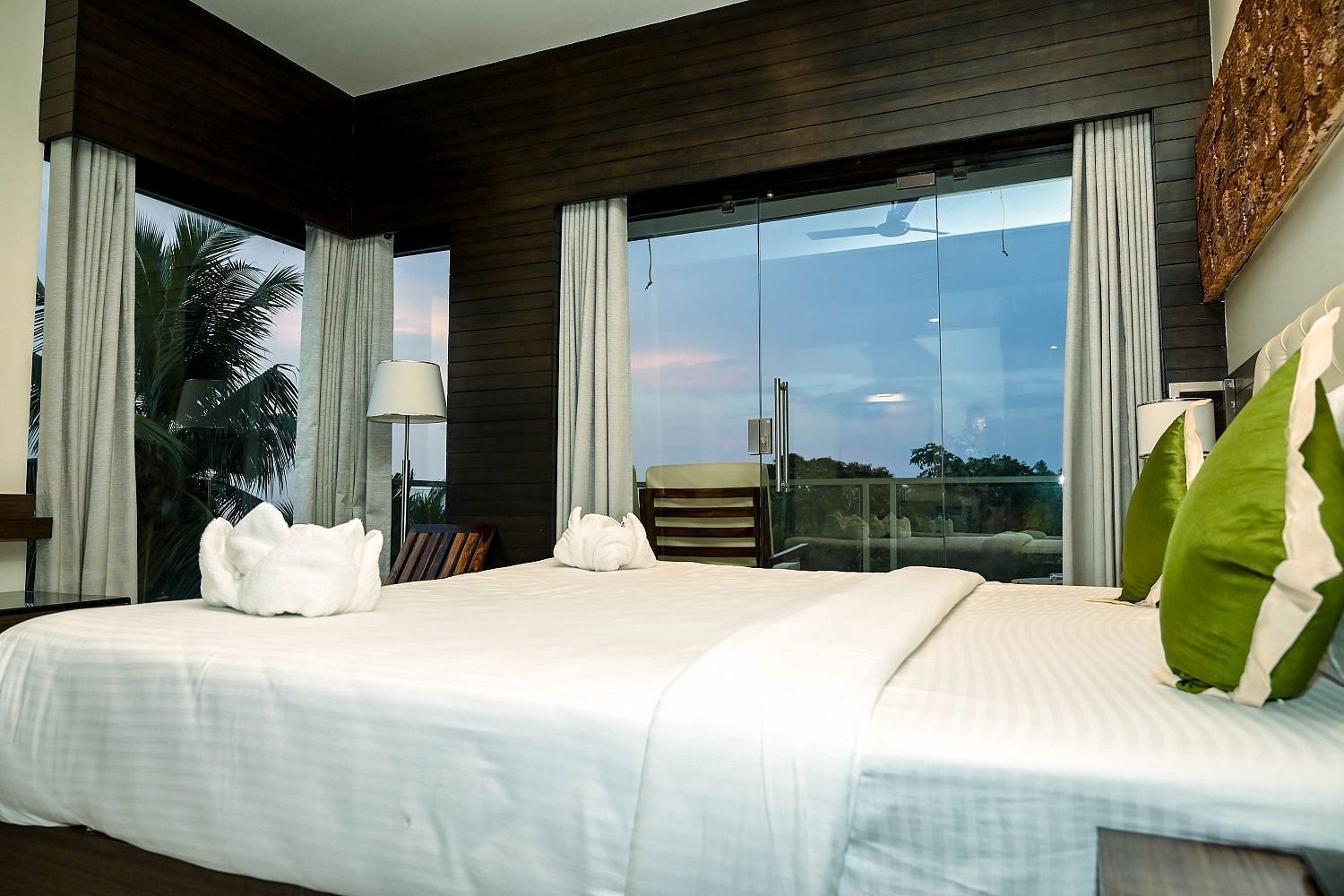 A bright hotel room with a large bed, decorative white towels shaped like swans, and a wide window offering a view of the surrounding tropical environment - Sea Hills Hotels, Sri Vijaya Puram (Port Blair)