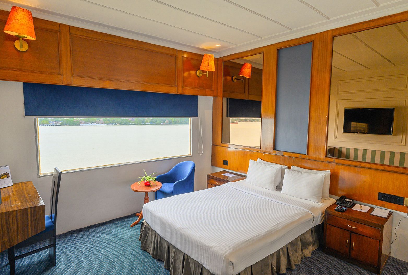 Double bedroom at Polo Floatel Kolkata with blue curtains, wooden paneling, and river-facing window.